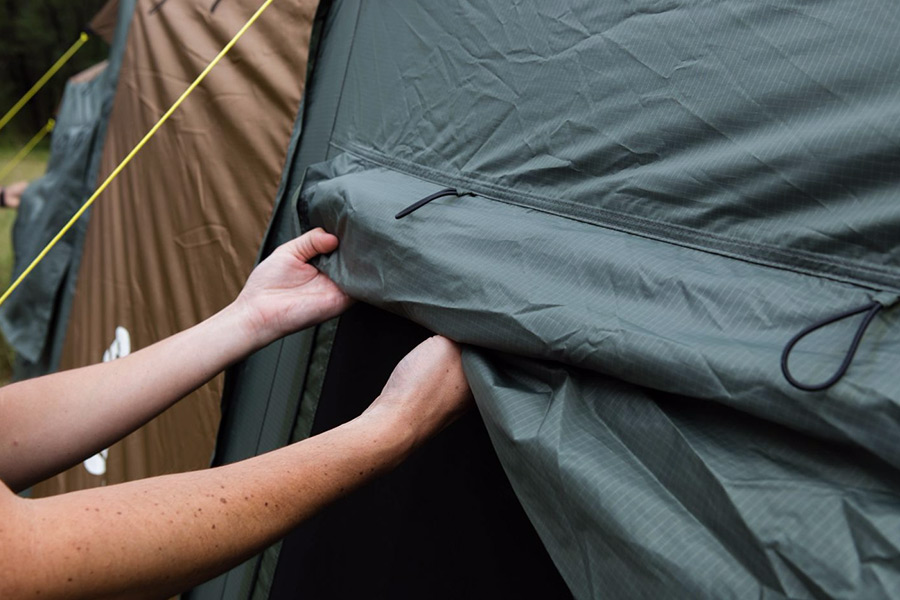 A person holding up a polyester tent fly on a Coleman tent