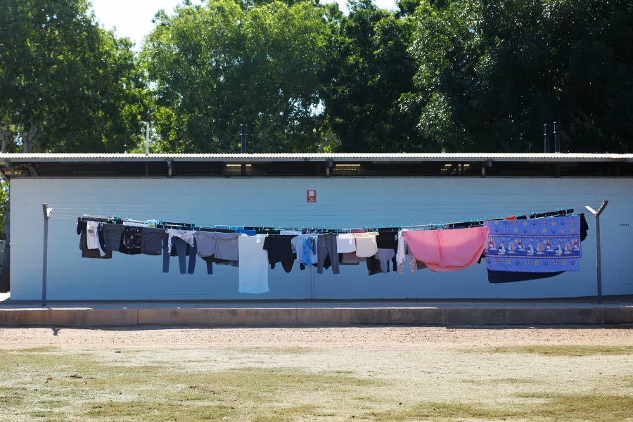 A load of washing hangs on a long clothes line in front of a toilet and laundry block
