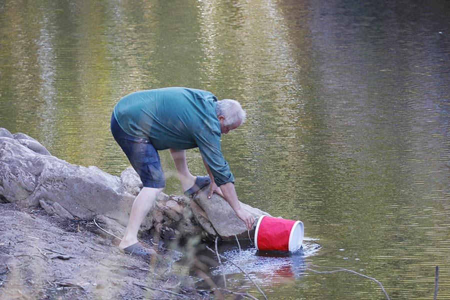 A man fills a bucket from a river