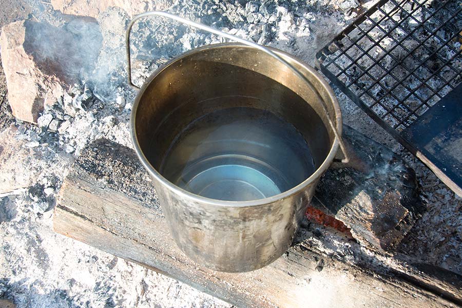 A metal bucket of water sitting next to a campfire