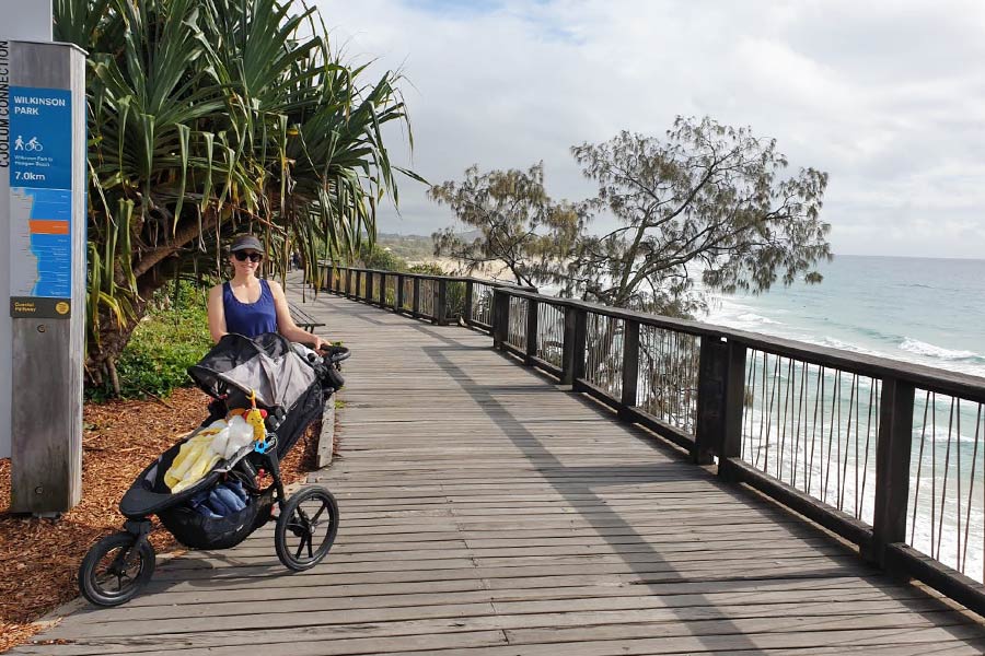 A woman with a stroller standing on a boardwalk next to the ocean