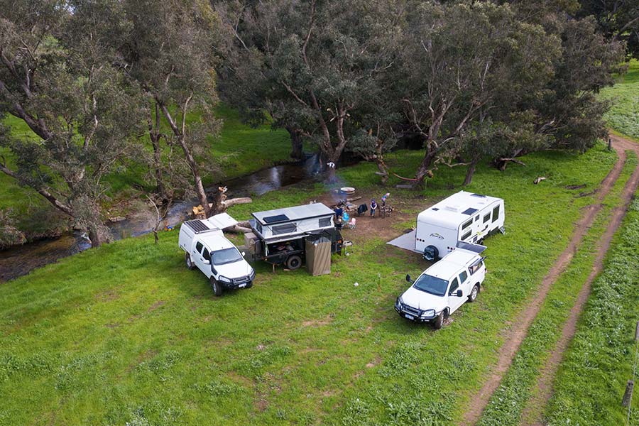 A drone photo of a campsite in a grassy area next to a flowing creek