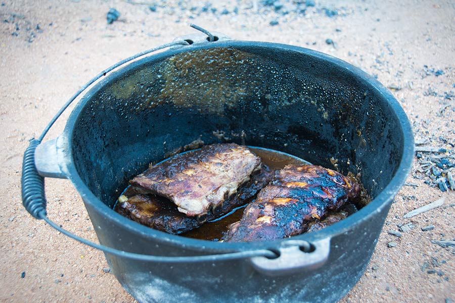 An open camp oven containing cooked pork ribs