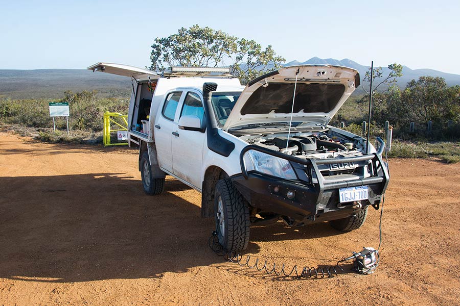 A 4WD vehicle parked on a dirt road with the bonnet open and an air pump connected to a tyre