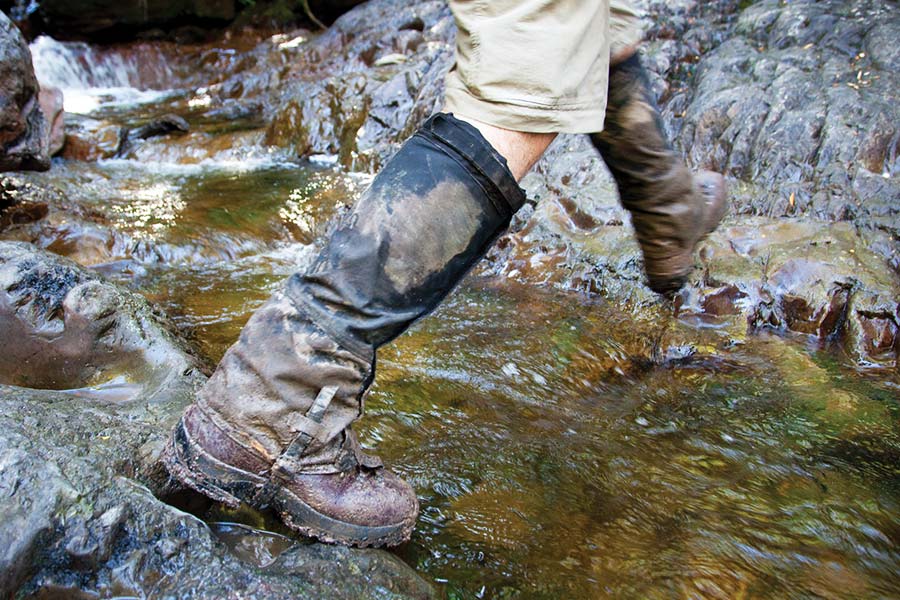 A person wearing gaiters as they step over a running stream of water