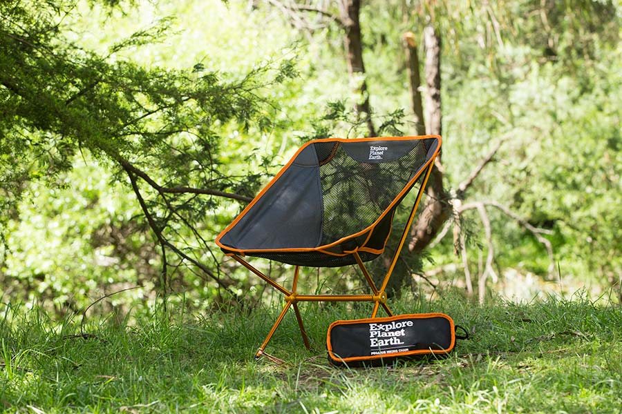 A lightweight hiking chair set up outdoors in a shady and grassy spot