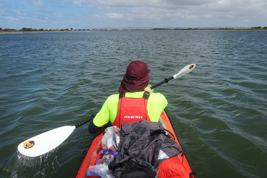 The back view of a person, sitting in the front of the kayak, paddling out across the lagoon.