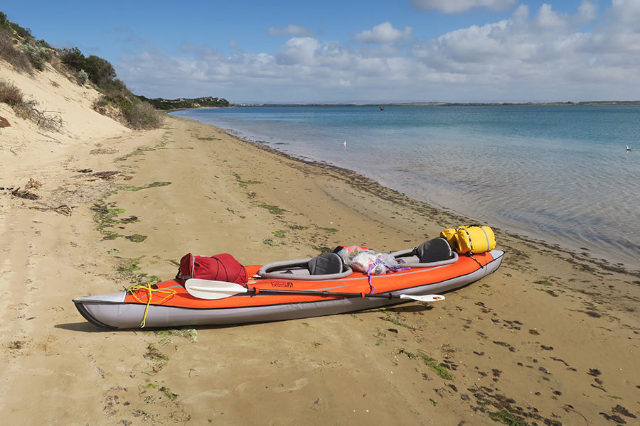 An orange and grey kayak sits on a sandy beach next to tall sand dunes.