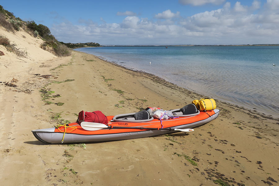 The northern side of the Younghusband Peninsula is sheltered from the wind. An orange and grey kayak sits on a sandy beach next to tall sand dunes.