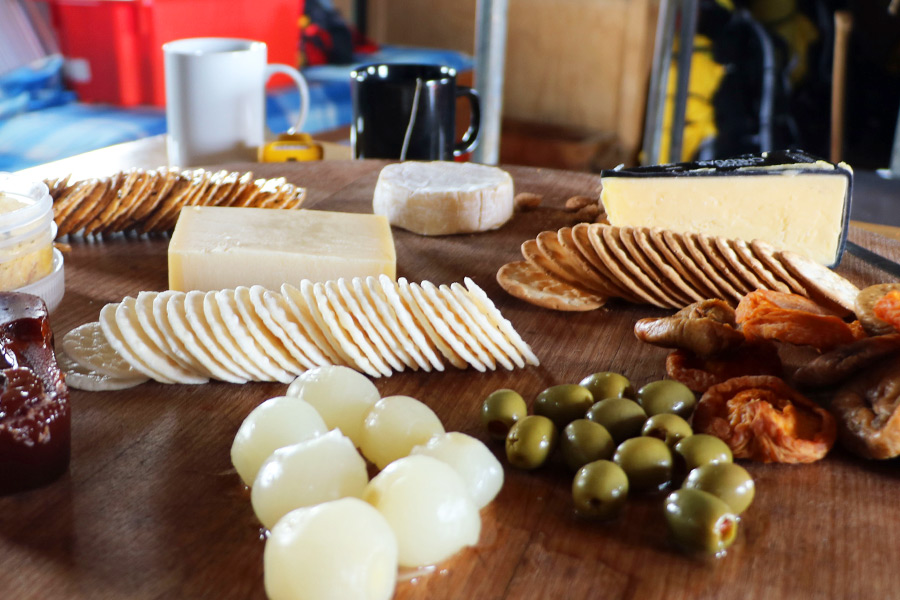 A spread of cheeses and antipasto on a wooden board.