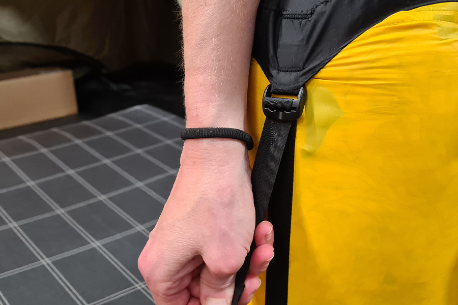 A hand pulls the black compression strap down on a yellow sack.