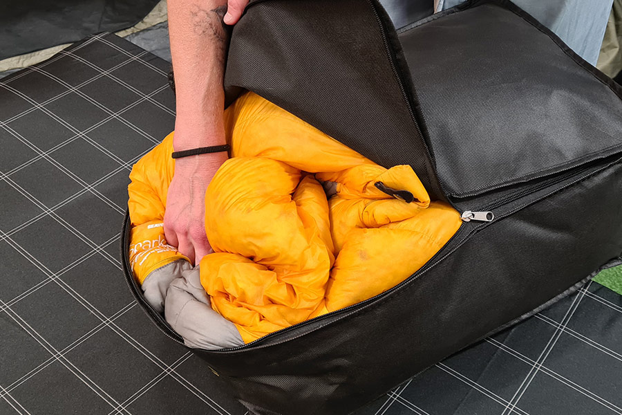 A Sea to Summit sleeping bag being stuffed into its loose fitting black storage bag.