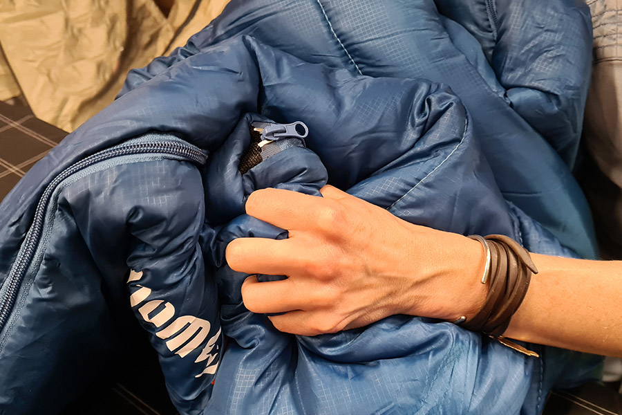 A hand grips and scrunches a handful of blue sleeping bag. 