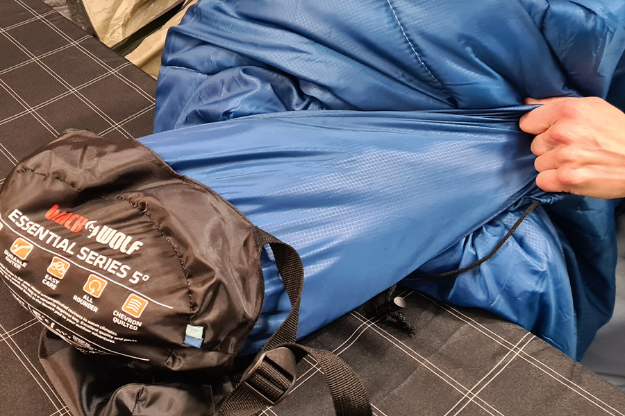 A hand stuffs a blue sleeping bag into a blue and black compression sack. 