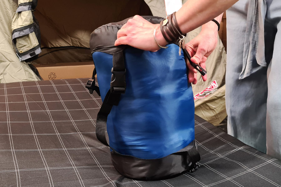 Hands fitting the black cap over the top of a blue compression sack