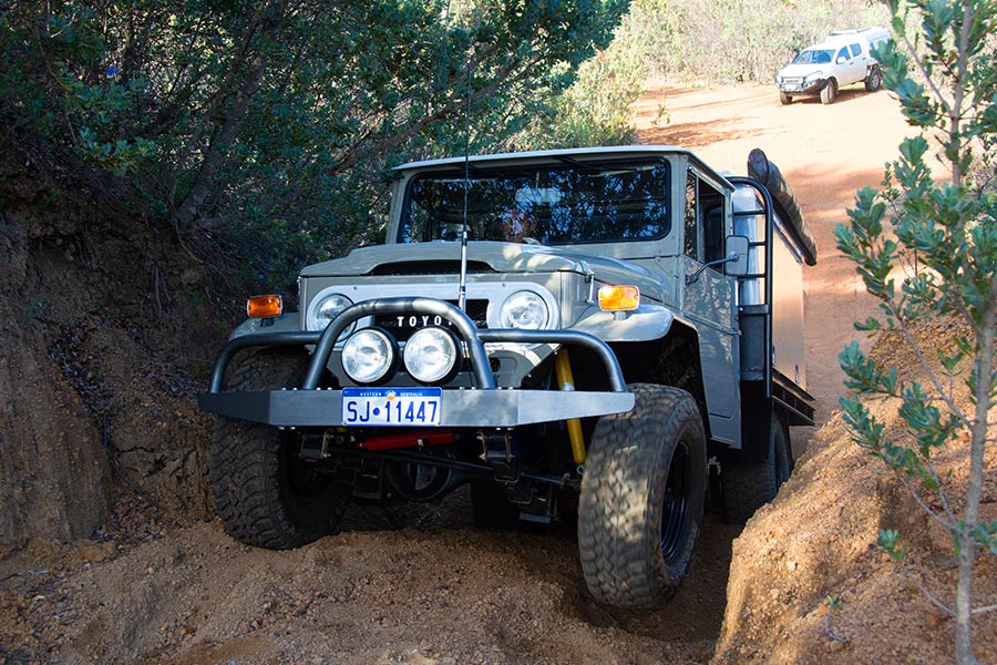 A close up of a Toyota Land Cruiser gets some air under the front right tyre as it negotiates a rough track.