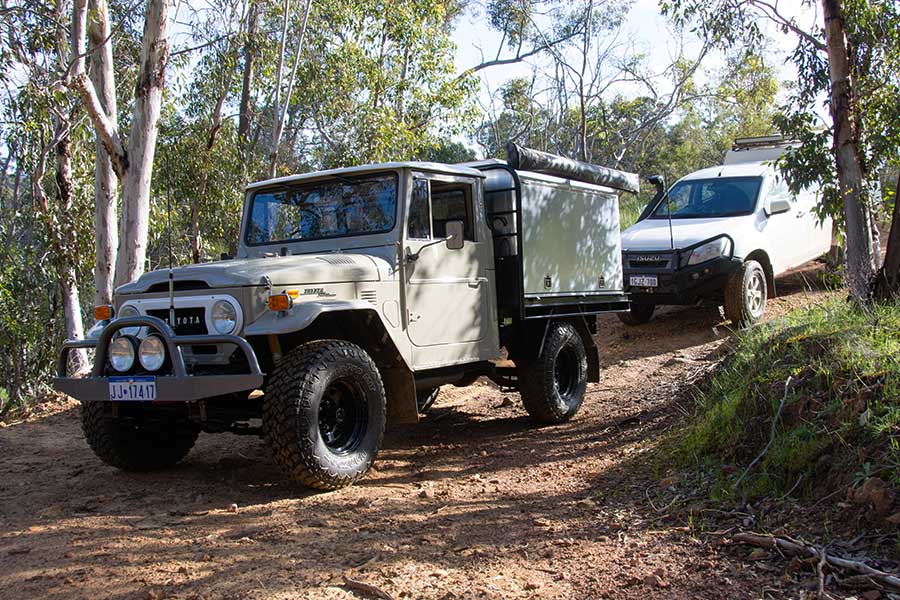 A Toyota Land Cruiser with modifications leads a white Isuzu on a 4WD track.