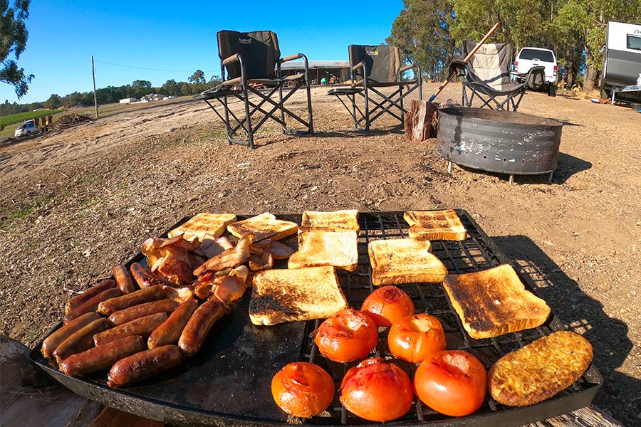 Sausages, bacon, tomatoes and toast cooking on a campfire grill.