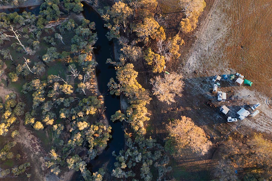 Aerial drone shot of a tree lined creek with a group of friends camped in a circle nearby.