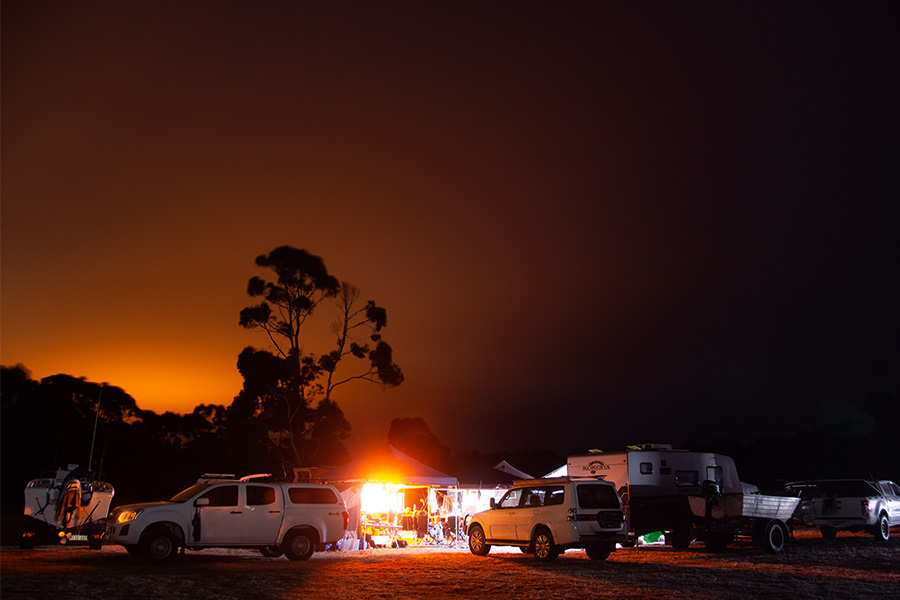 A camping group afetr dark with orange 12V lighting casting a glow over the 4WDs, boast gazebo and caravans.