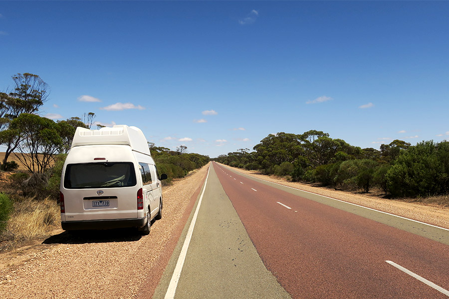 A white campervan pulled to the side of an outback Australian highway.