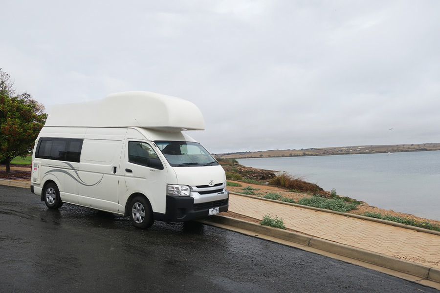 A white campervan parked to the side of the road overlooking Streaky Bay. It's a rainy day with thick grey cloud.