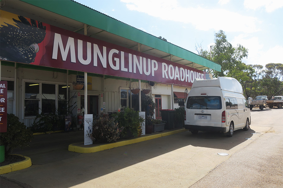 Out the front of the Munglinup Roadhouse with large signage and a white campervan parked by the bowser.