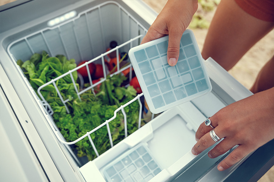 The inside of a portable fridge with the baskets full of fresh produce. A woman's hands are retrieving a plastic container.