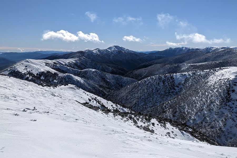 A snow-capped mountainous vista with clear blue sky and a few scattered white clouds.