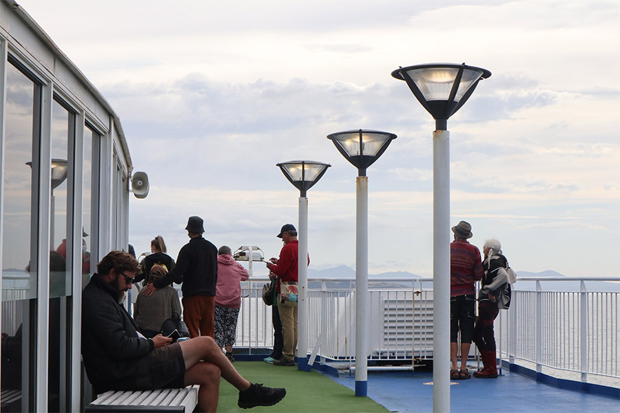 An outdoor area on a ferry with a few people scattered about. 