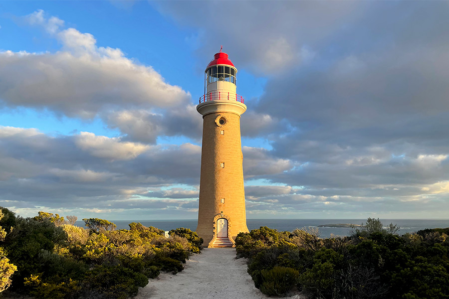 The lighthouse at Cape de Coudic. There's patchy cloud across the sky and the setting sun is casting golden light upon the lighthouse.