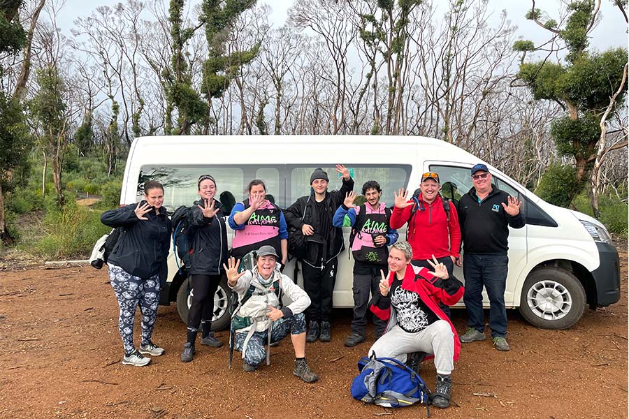 This was an adventure we will all remember. Nine people in hiking gear are gathered in front of a minivan having been dropped of at the start of a trail.