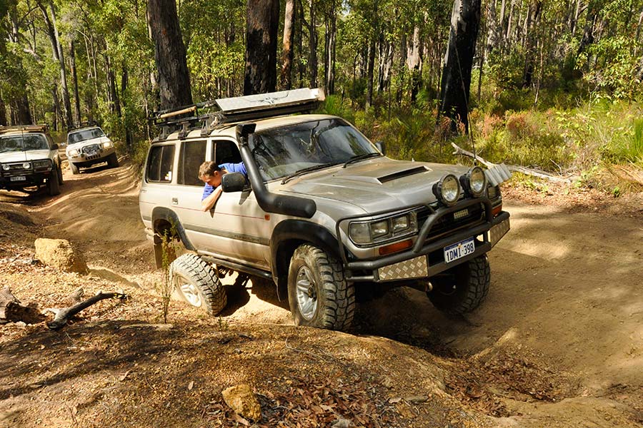 A well kitted out 4WD vehicle navigating a rough track with a couple of mates behind.