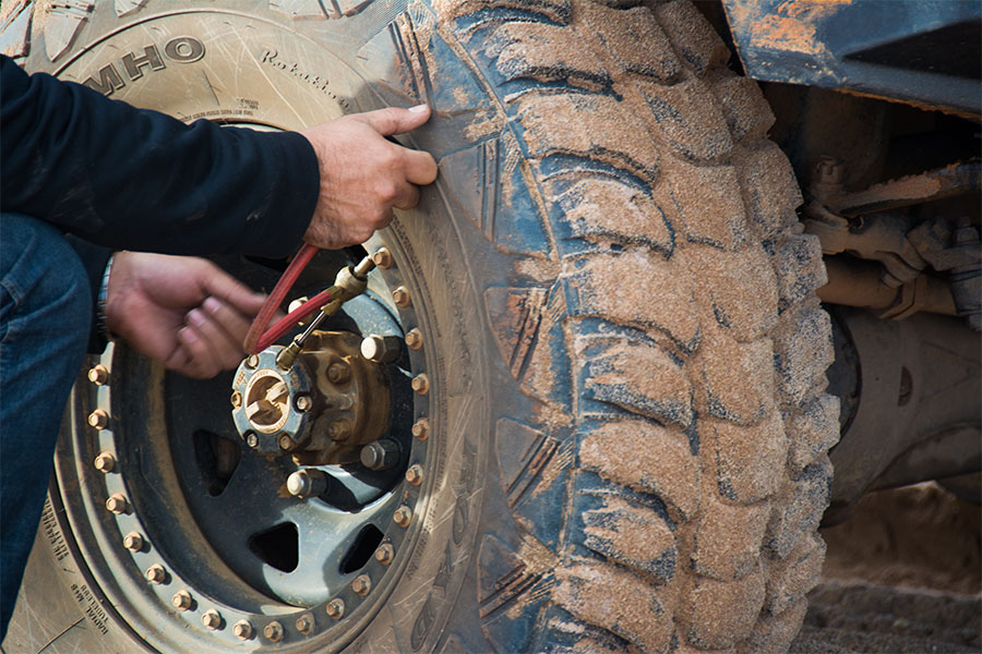 Close up of an off-road tyre with sand in the tread. A man's hands are deflating the tyre.