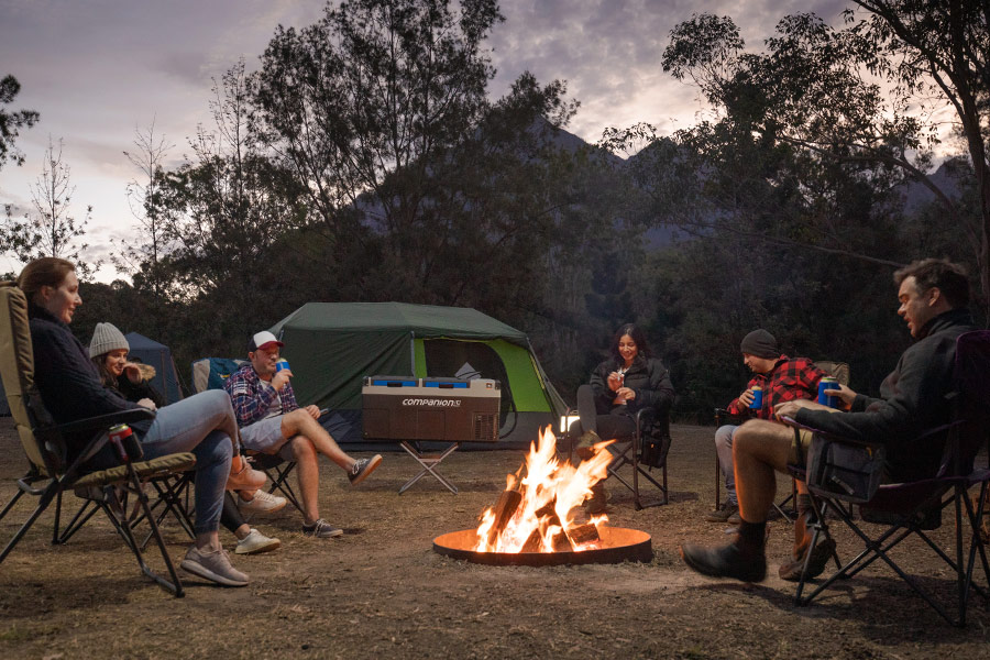 A group of friends, sitting around a campfire at a campsite.