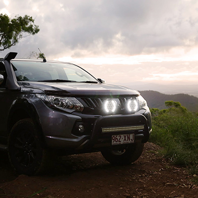 The front of a 4WD vehicle in the High Country with two Hard Korr Driving Lights illuminated against a cloudy backdrop.
