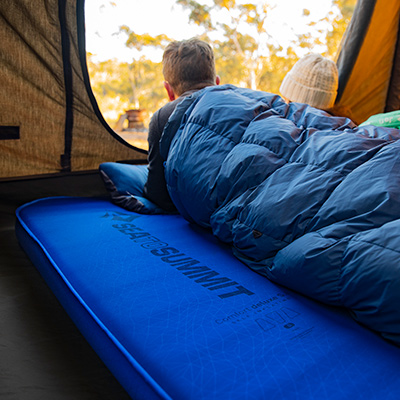 A couple using a complete Sea to Summit sleep system are lying inside their sleeping bags and looking out the open door of their touring tent.
