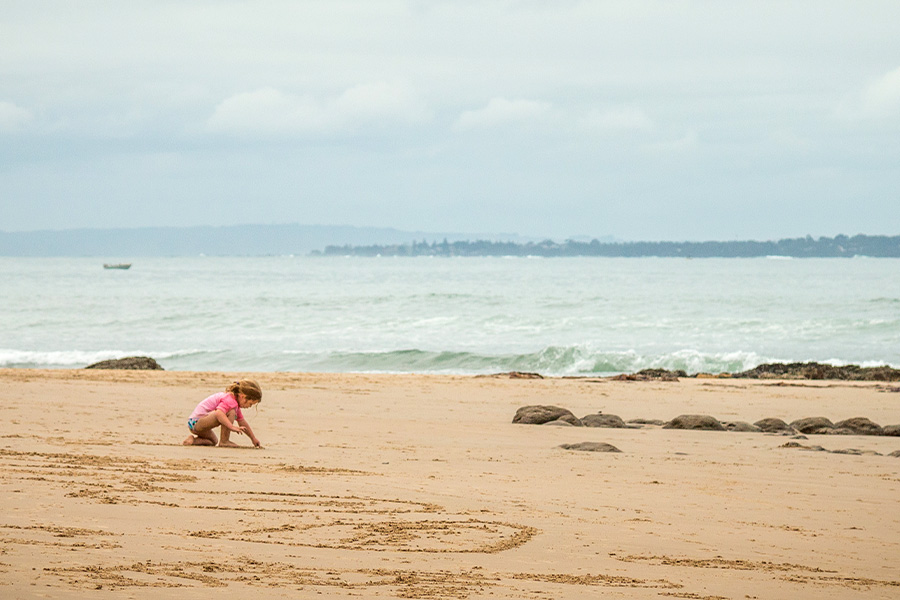 A young girl draws in the sand at the beach. It looks to be a cloudy and windy day.