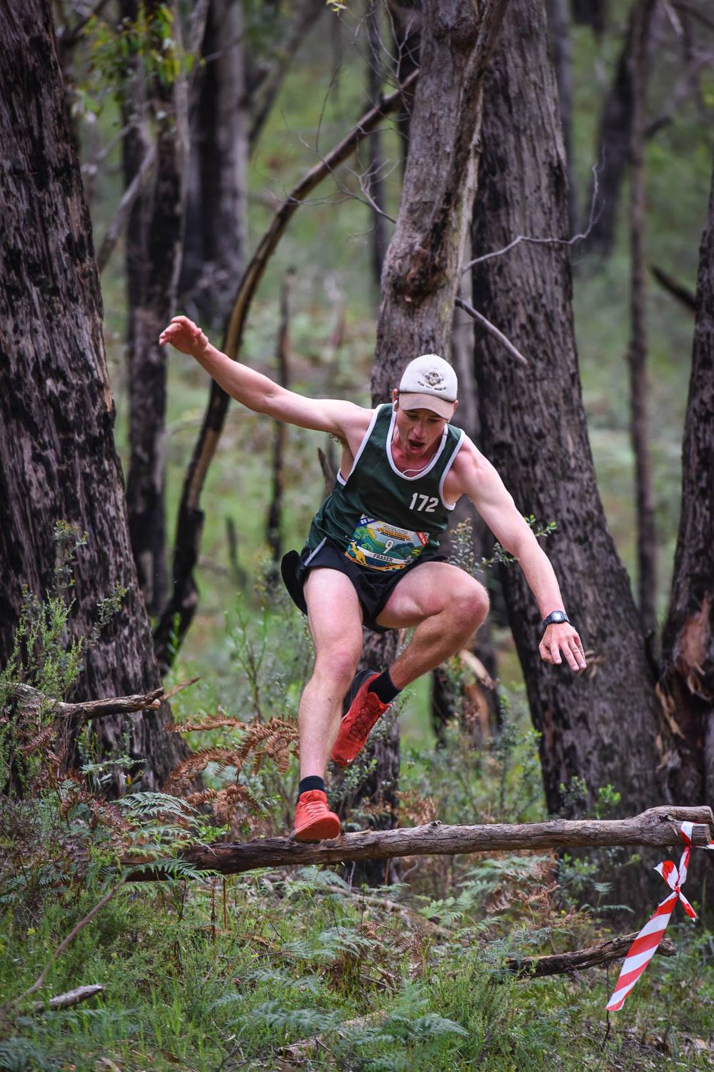 A male trail runner leaping over a fallen branch.