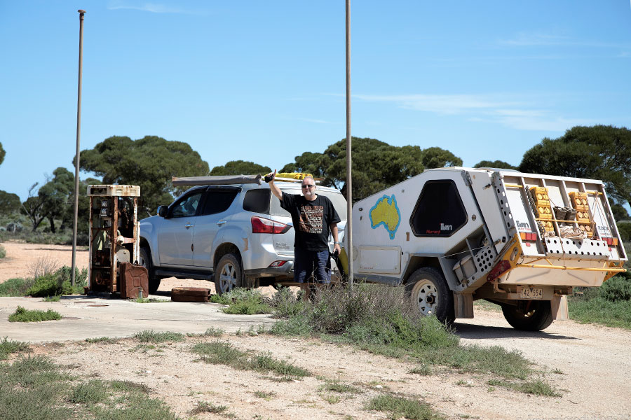 Man waving to the camera and standing in front of a 4WD towing a Tvan that's pulled to the side of a country road.