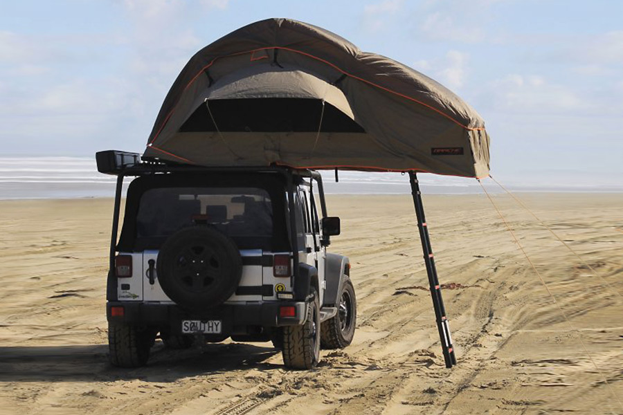 A Jeep packed on sand near the ocean with a roof top tent set up.