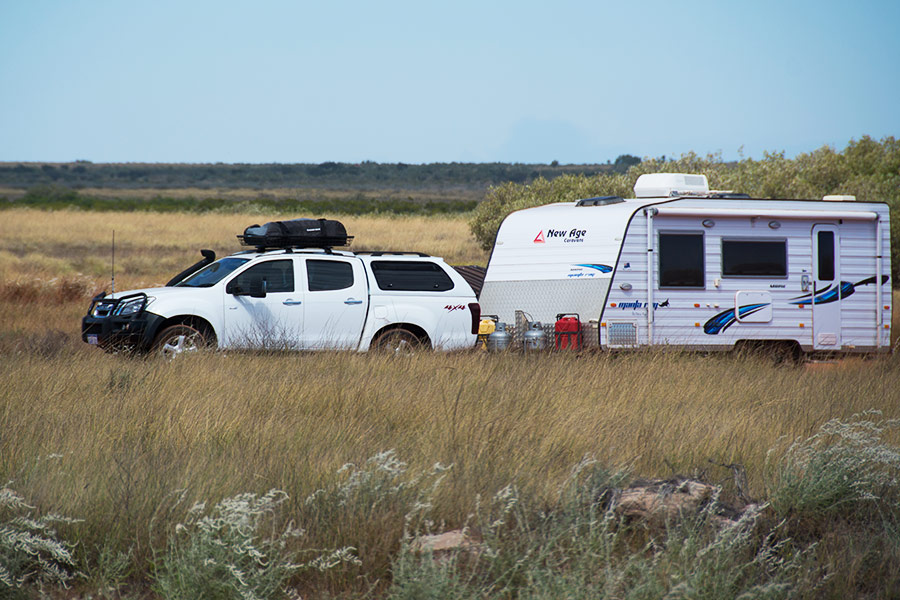 A 4WD towing a large white caravan along a country road.