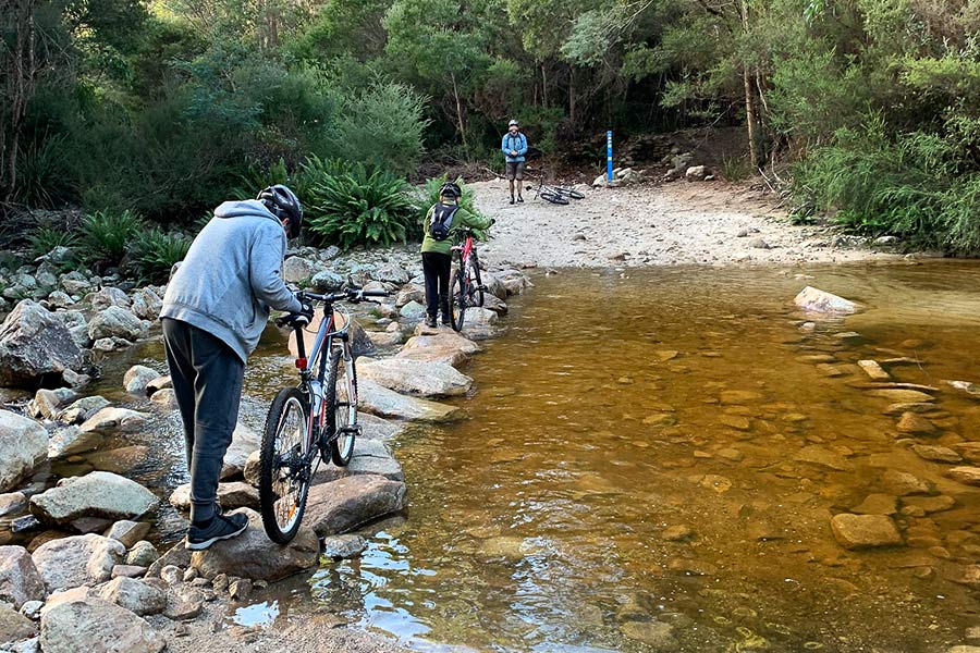 Derby's ‘green’ trails were both appropriately rated and consistent with what we’d consider the same back home. Three cyclists are wheeling their bikes over the rocks the create a stepping-stone bridge across a yellowing, shallow creek.