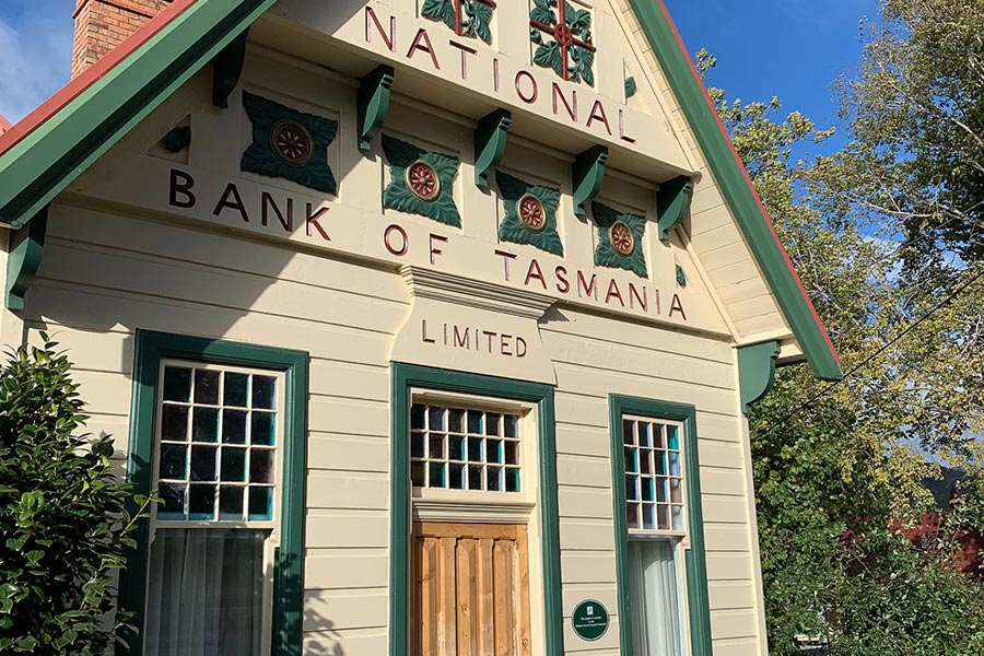 The National Bank of Tasmania The National Bank of Tasmania - a cream house-like building, with dark green and red trims and a golden-wood door. The roof is red, and the chimney is red brick.