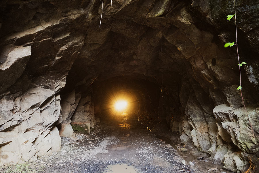 The opening to a dark rocky cave presents a bright, orange beacon of light at the end, indicating the end of the tunnel. 