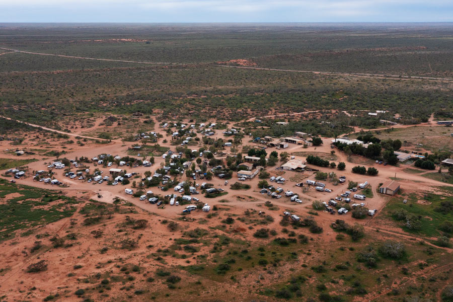 A overhead shot of Ballara Station shows rich, red land patched with various shades of green shrubbery. There are cars and camp vehicles peppered in the centre of the frame suggesting a busy campsite. 