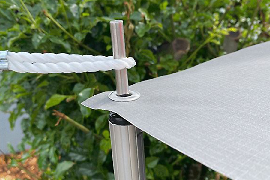 A guy rope is looped onto a silver spigot, which pokes through an eyelet in the corner of a grey tarp. 