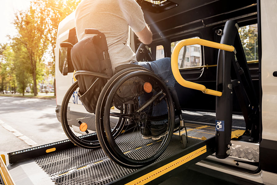 A man in a wheelchair is being levered on a ramp into the a van-like vehicle via the side doors. 