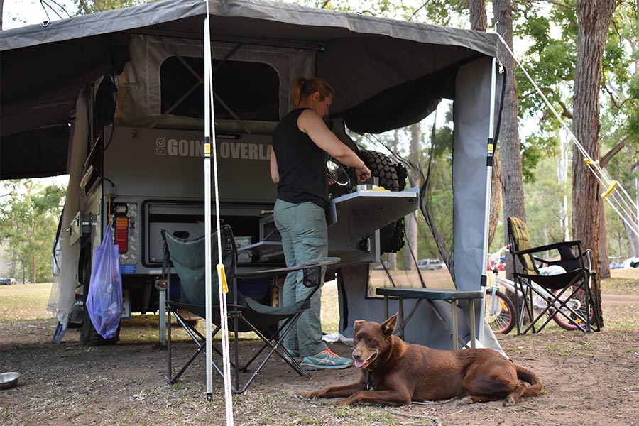 Woman cooking on the grill with her dog lying down next to her.