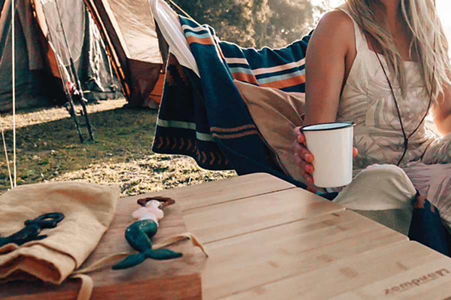 A lady is sitting at a camp table holding a cup.